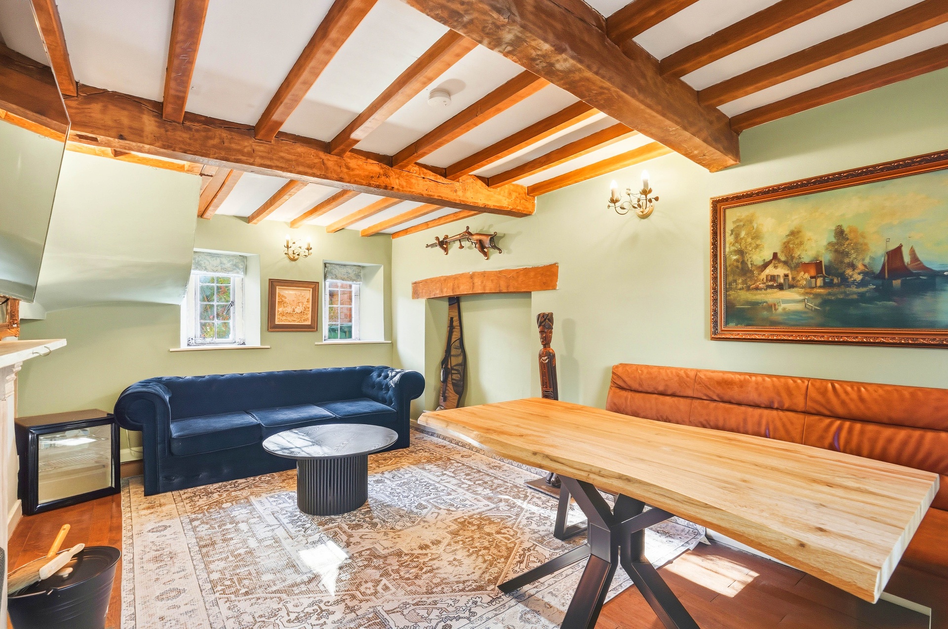 Mae Cottage sitting room with exposed beams, sage green walls, navy chesterfield sofa and live-edge dining table